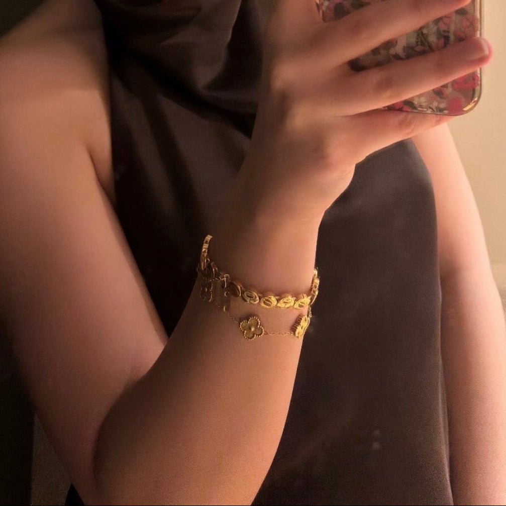 Woman holding a phone with a floral case, wearing a brown scarf and gold bracelet.
