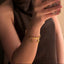 Woman holding a phone with a floral case, wearing a brown scarf and gold bracelet.