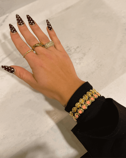Hand with polka dot nail polish wearing multiple rings and a peach and lemon cocktail bracelet on a light background