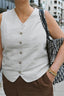 Person wearing a light gray vest over a white shirt with brown pants, holding a patterned bag - wearing AV Jewels Cross necklace