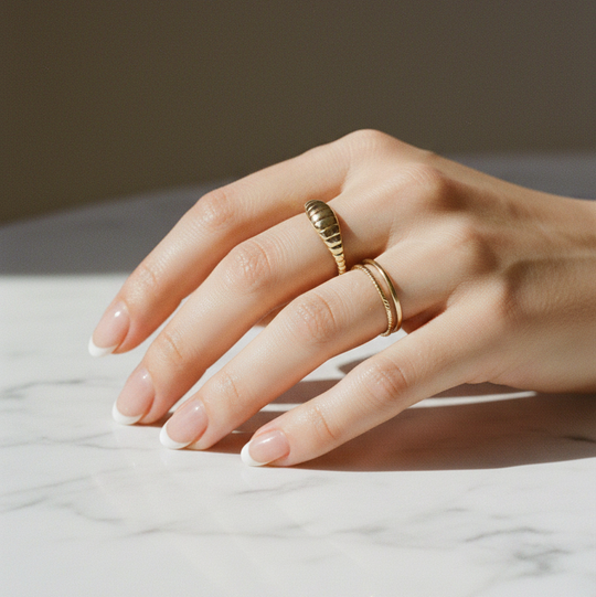 Hand wearing two gold rings on a marble surface with a neutral background and she  has the mini croissant ring on from AV Jewels Jewelry
