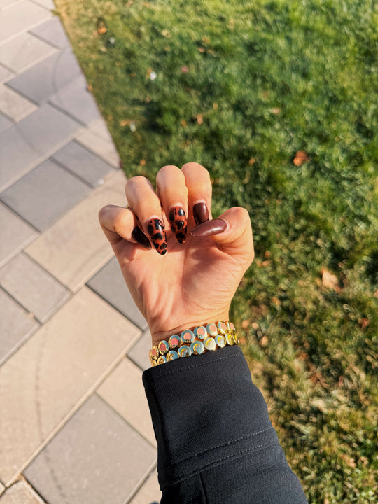 Hand with patterned nails and AV Jewels cocktail club bracelets against a grassy background