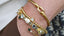 Gold bracelets with various charms on a wrist against a neutral background